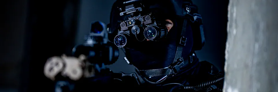 Militair in het donker met helm en Photonis-nachtzichtkijker richt een wapen